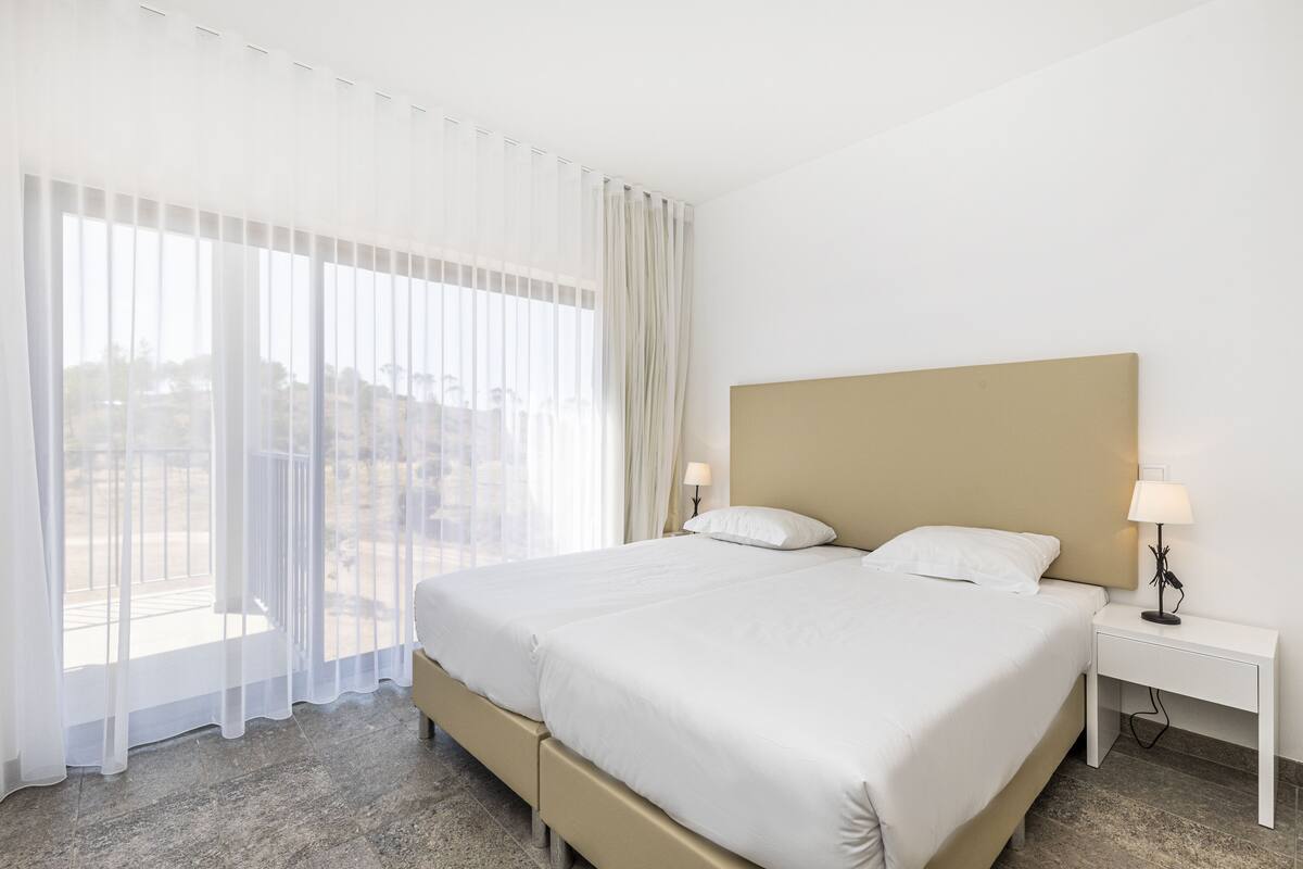 Une chambre d’hôtel avec un grand lit, deux tables de chevet et des rideaux légers.