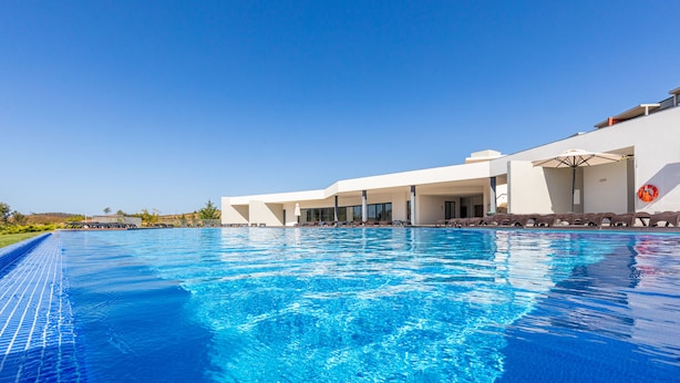 Um hotel moderno com piscina, espreguiçadeiras e um céu azul límpido.
