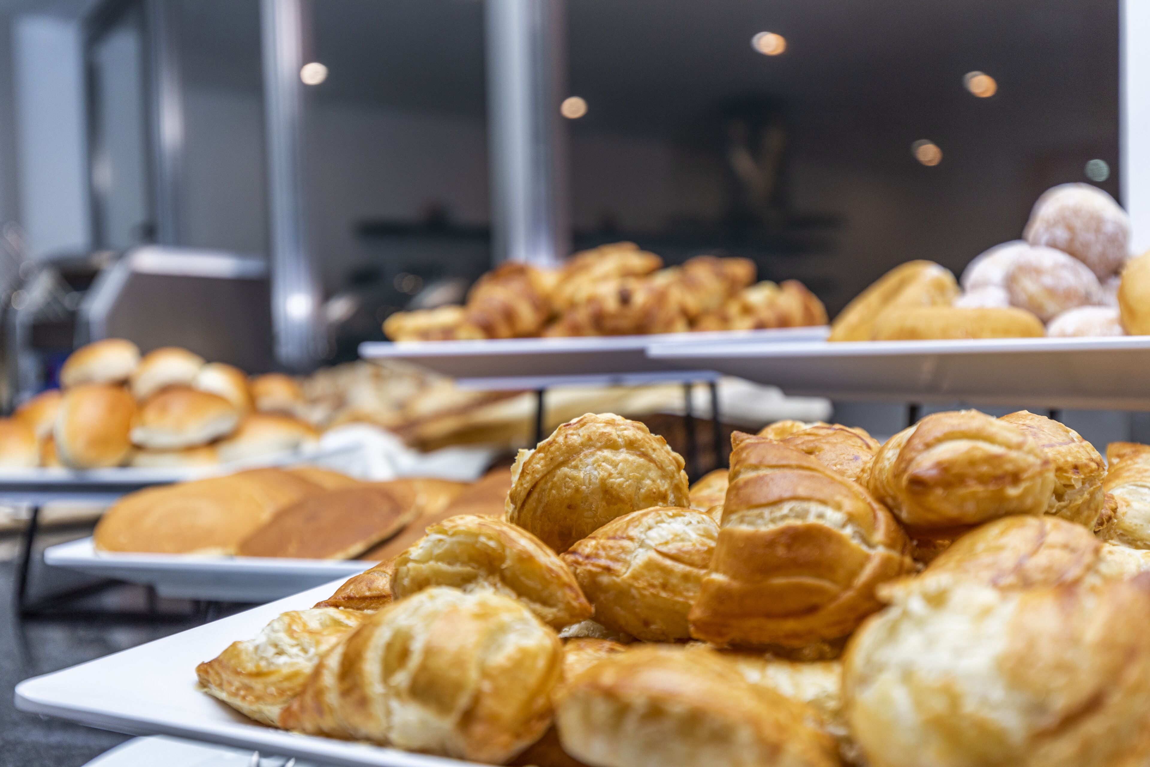 A variety of pastries on display, including croissants and other baked goods, arranged on white plates.