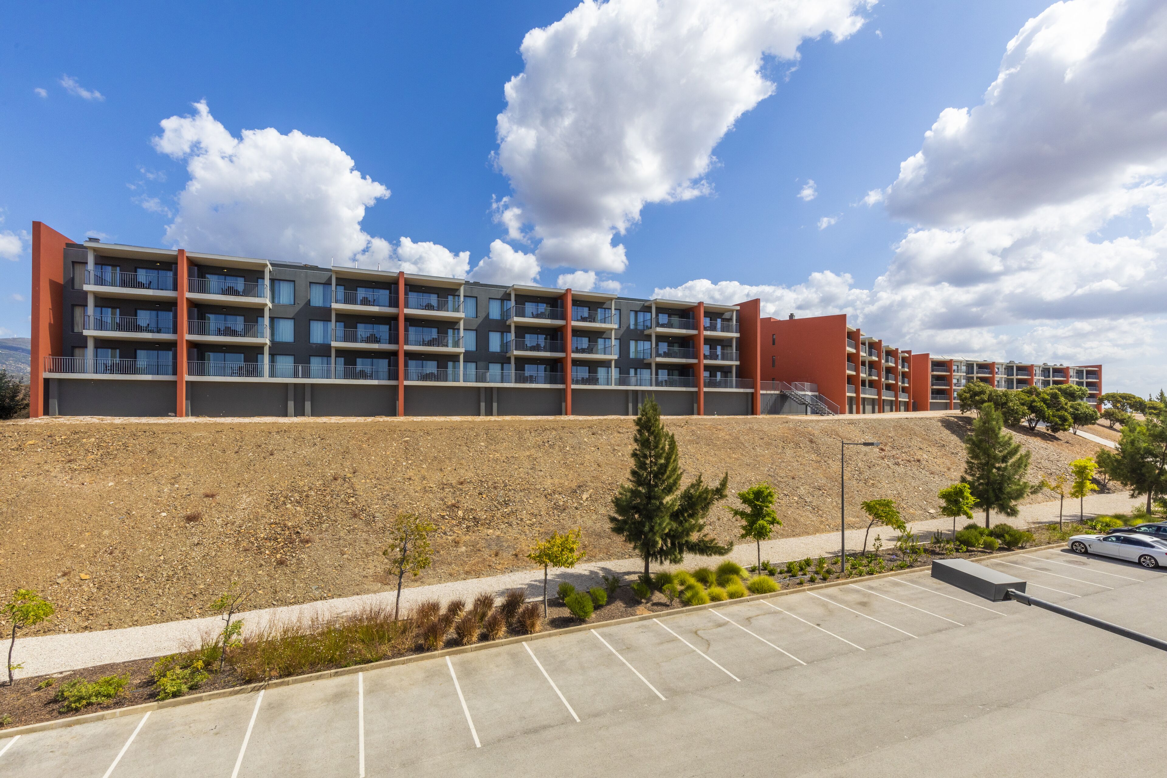 A multi-story parking structure adjacent to a modern building with balconies and a landscaped area with small trees.