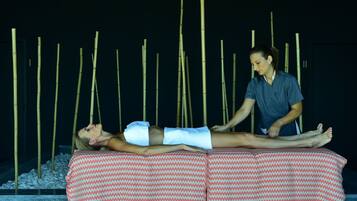 A person receiving a massage on a bed with a patterned cover, in a room with bamboo sticks in the background.