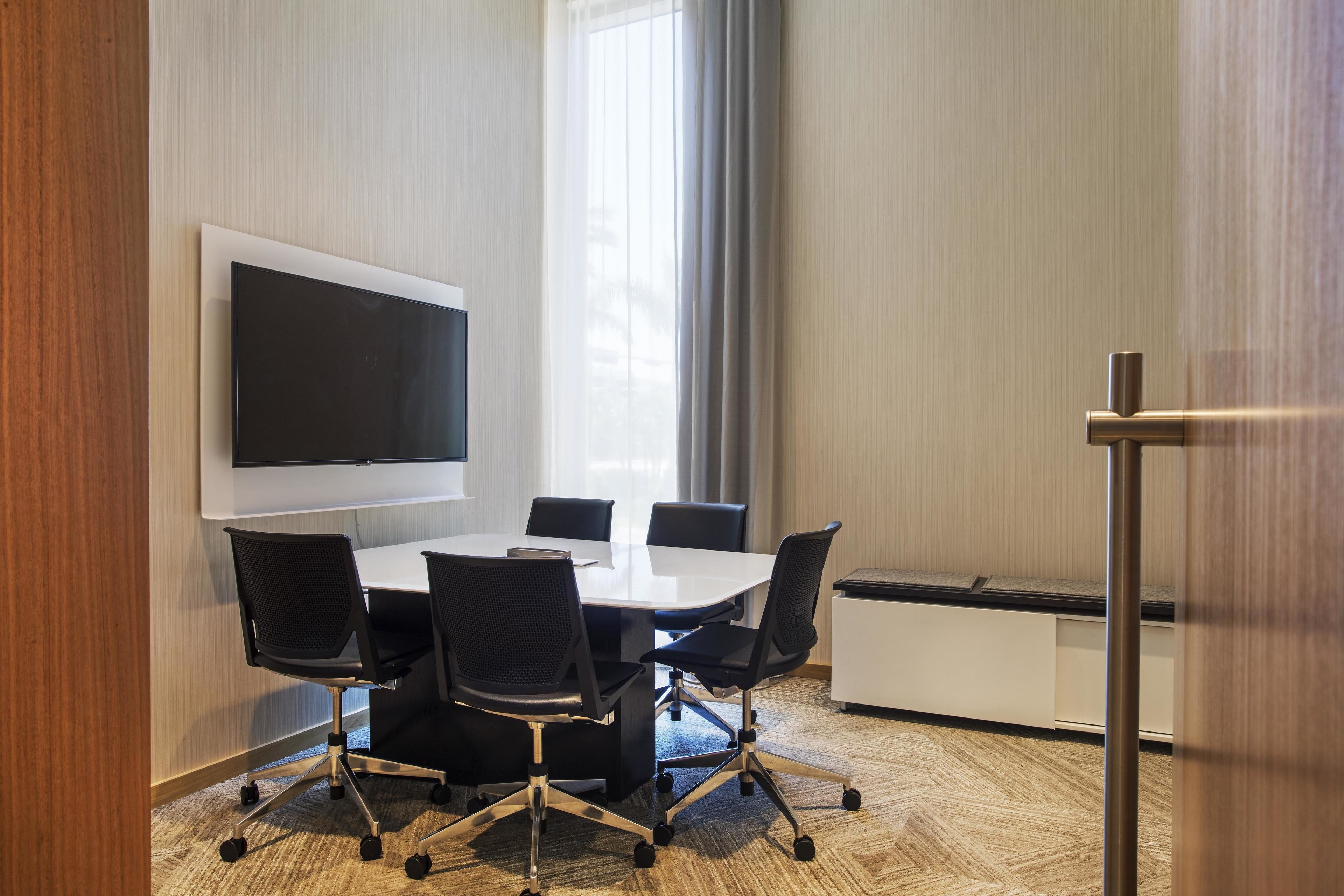 Una sala de conferencias con una amplia pantalla plana, una mesa blanca y sillas de oficina negras.