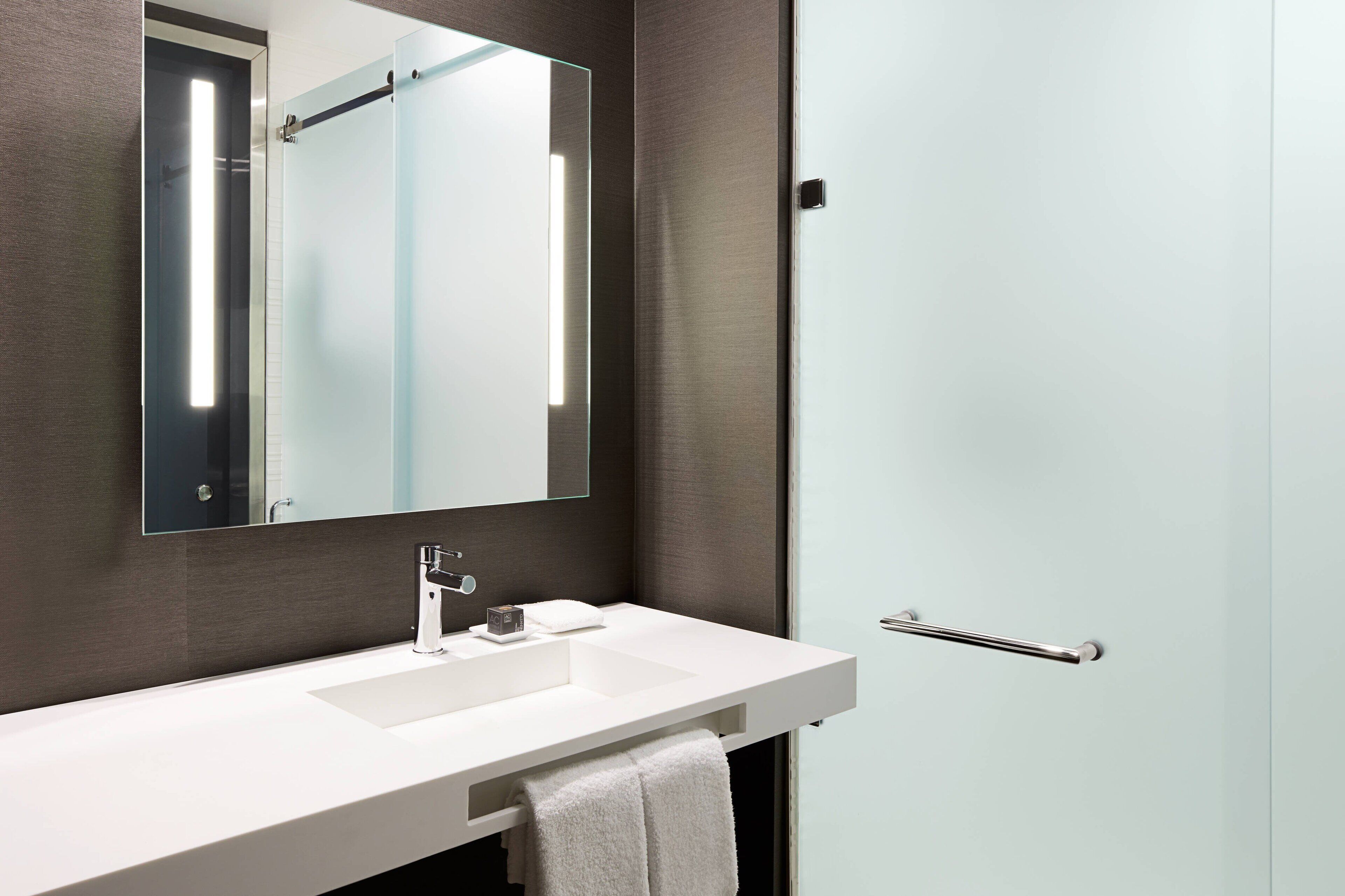 Ein modernes Badezimmer mit einem weißen Waschbecken, einem großen Spiegel und einem Handtuch an der Wand.