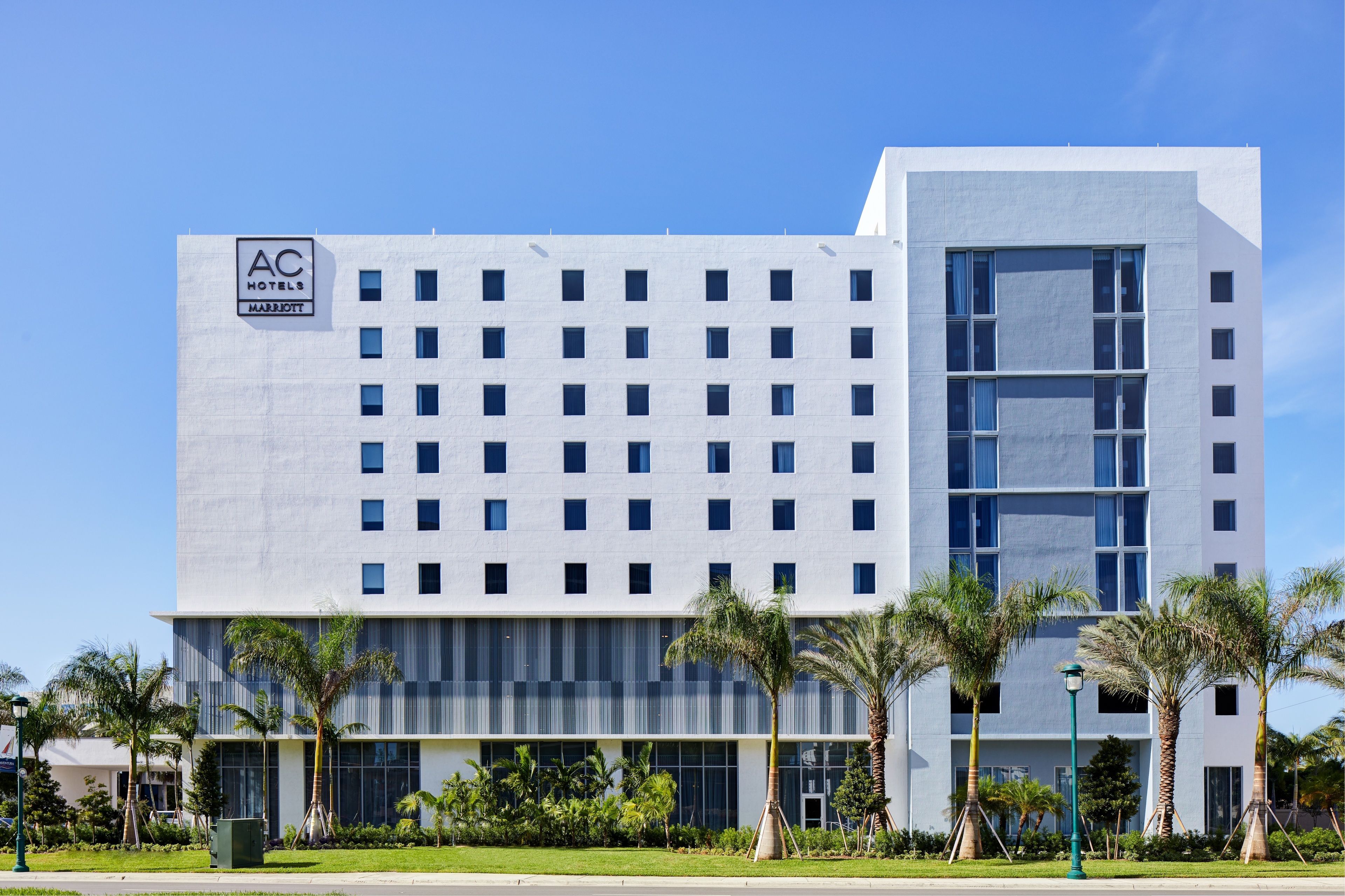 A modern hotel building with a grid of windows, a large glass entrance, and palm trees in the foreground.
