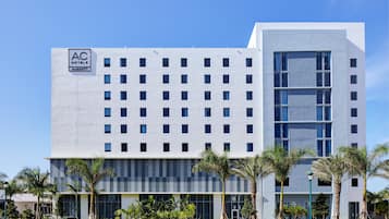 A modern hotel building with a grid of windows, a large glass entrance, and palm trees in the foreground.