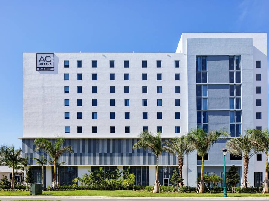 A modern hotel building with a grid of windows, a large glass entrance, and palm trees in the foreground.
