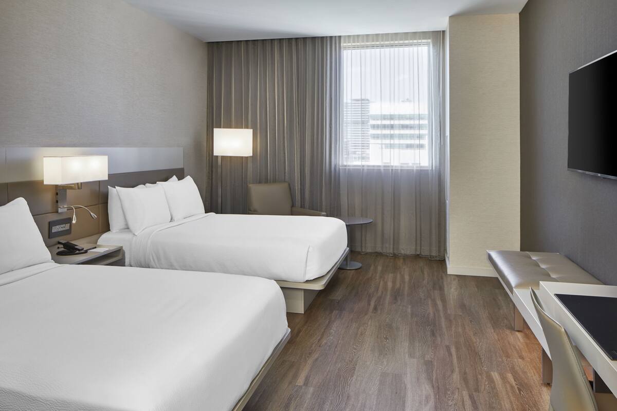 Une chambre d’hôtel avec deux lits, un bureau, une chaise, une télévision et une fenêtre avec des rideaux.