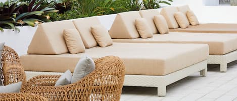Ein moderner Außenbereich mit einer Sitzecke, einer Couch und Korbstühlen, umgeben von üppigem Grün.