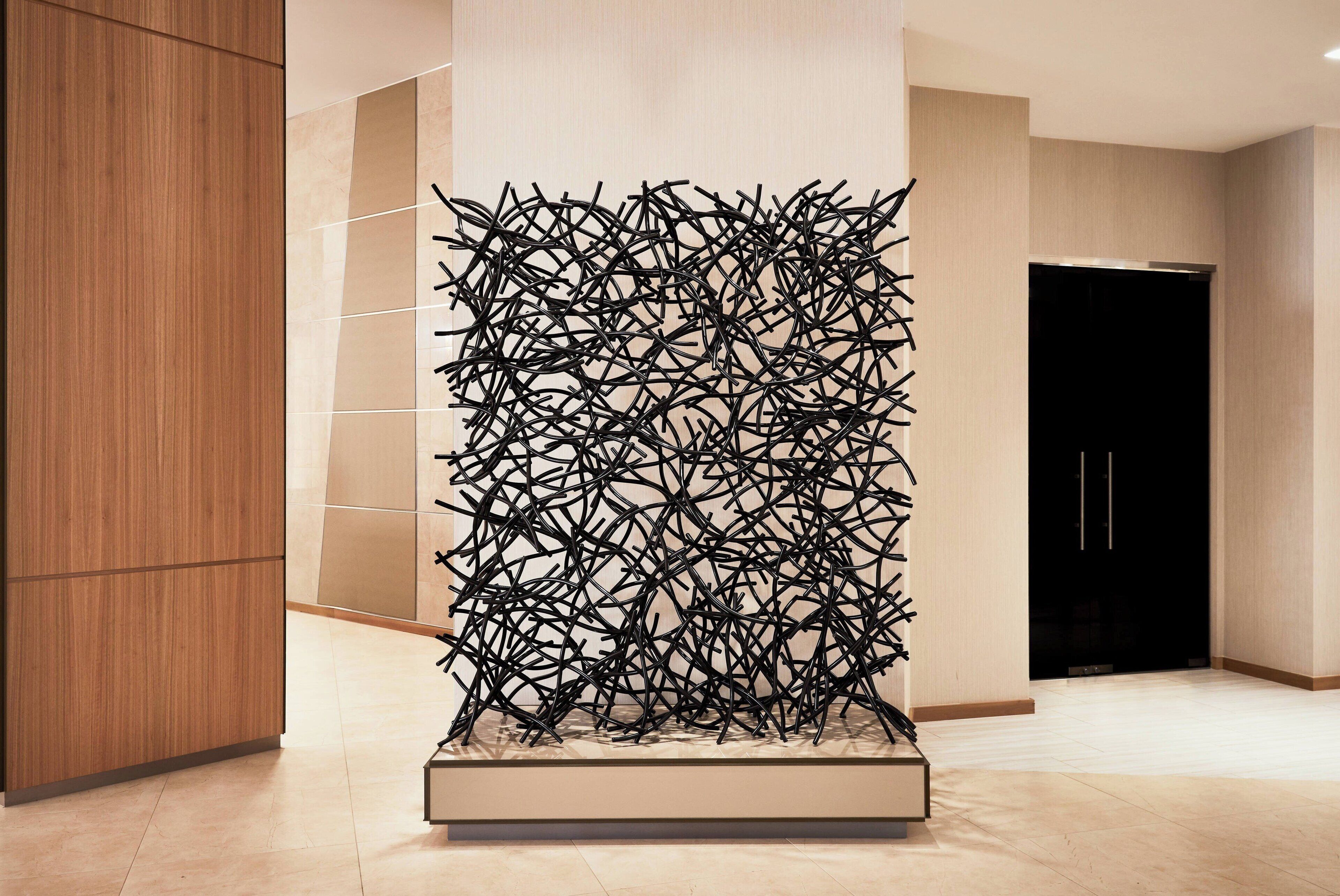 Um interior moderno com uma escultura abstrata preta e singular no centro, um painel de madeira à esquerda e uma porta preta ao fundo.