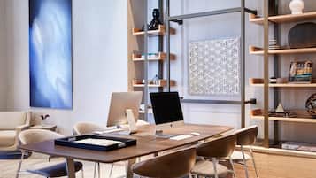 A modern conference room with a wooden table, two Apple iMacs, a large abstract painting, and a decorative geometric wall panel.