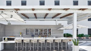 An outdoor bar area with a white counter, multiple bar stools, and a variety of bottles and glasses.