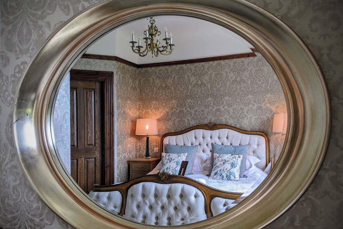 A bedroom with a large round mirror, a bed with tufted headboard, two bedside lamps, and a chandelier.