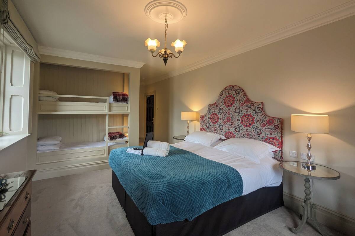 A bedroom with bunk beds, a large bed with a patterned headboard, bedside lamps, and a chandelier.