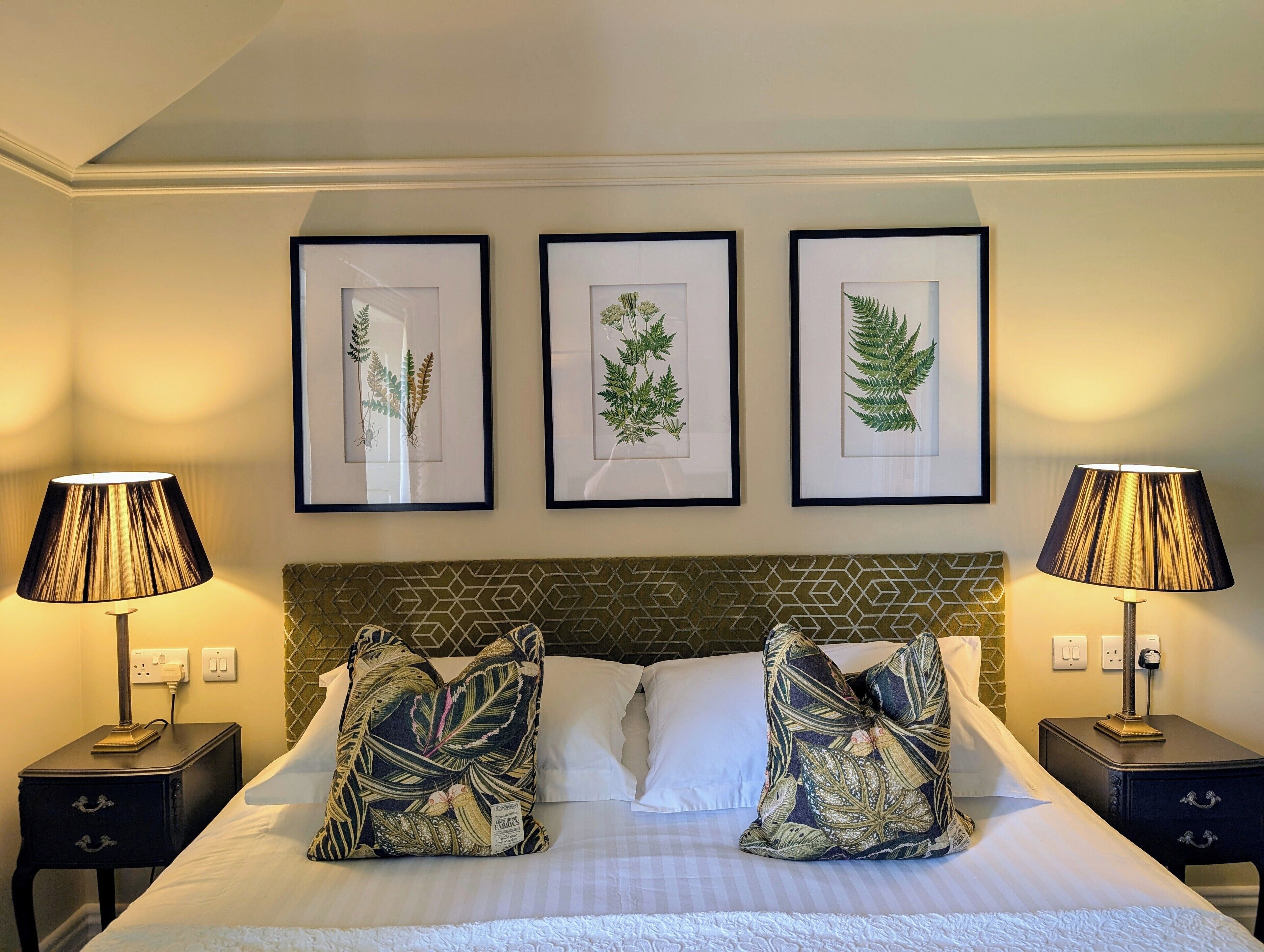 A hotel room with a bed, two nightstands, and three framed botanical prints on the wall.