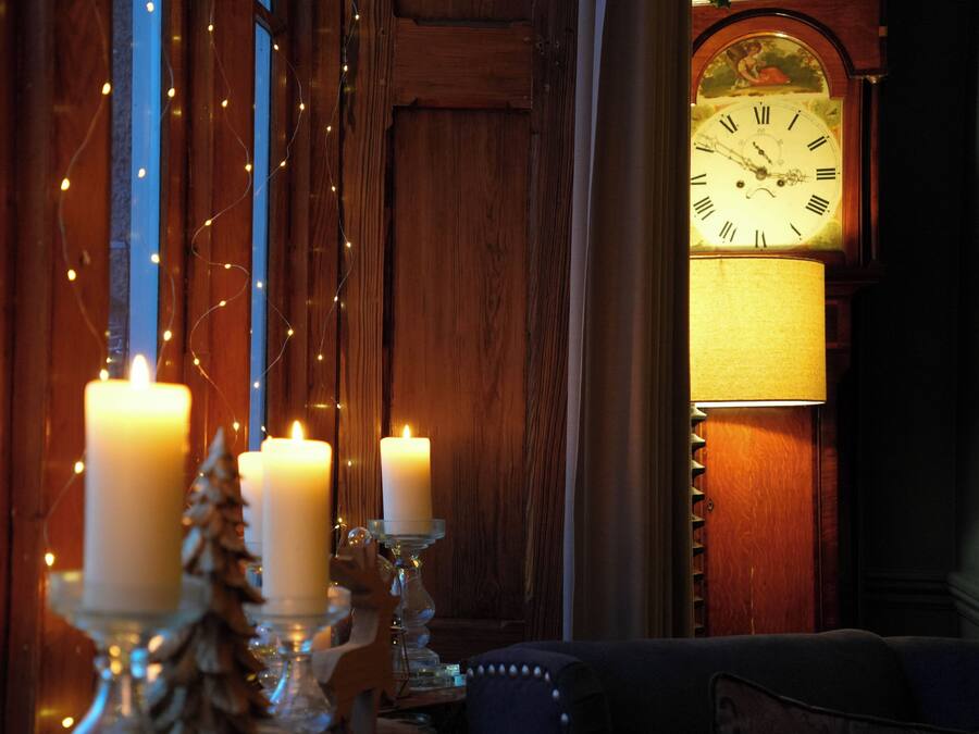 A cozy room with a wooden wall, a large clock, and three lit candles.