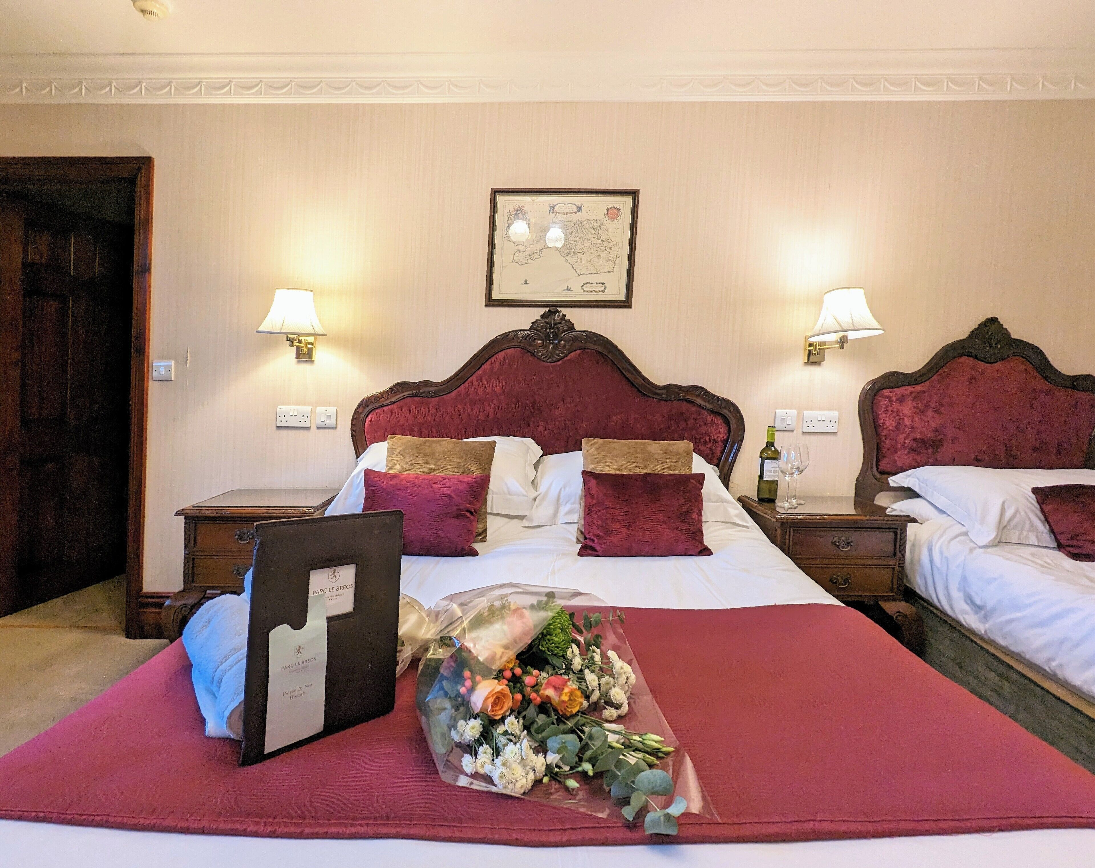 A hotel room with a large bed, two nightstands, a framed map on the wall, and a bouquet of flowers on the bed.