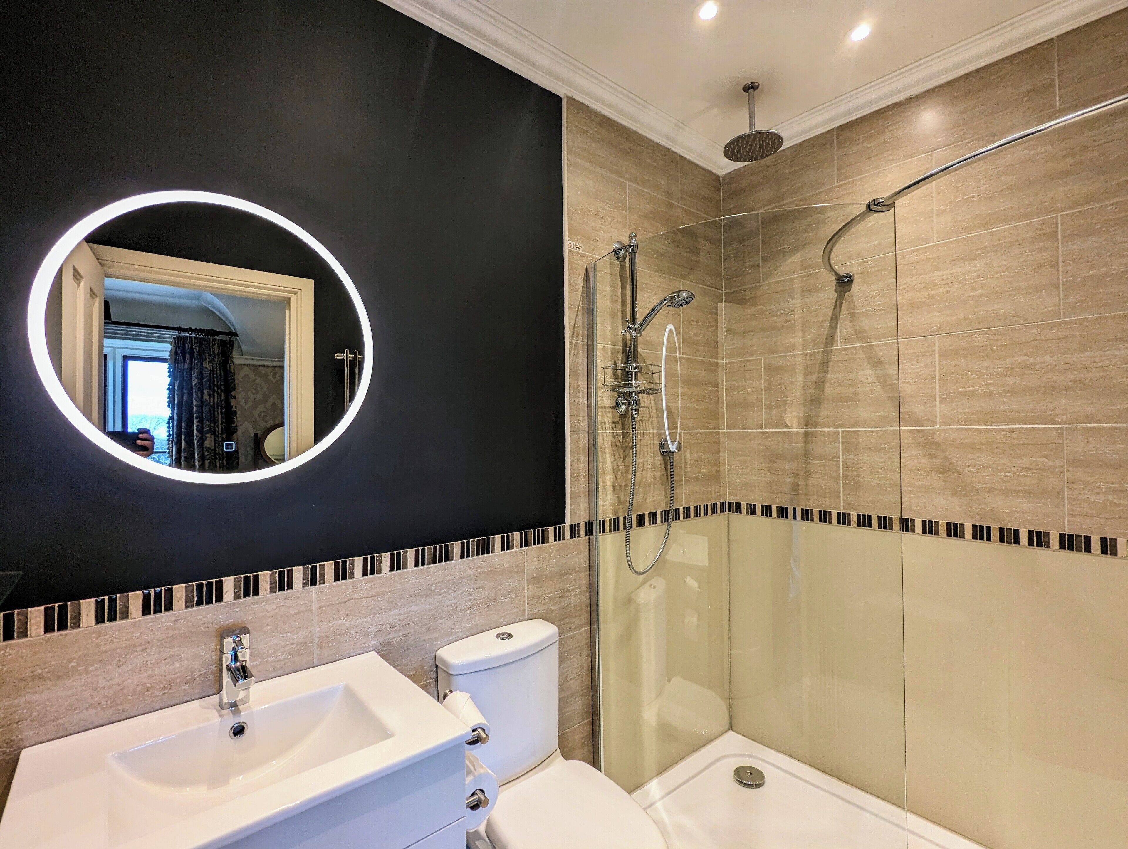 A modern bathroom with a round mirror, a shower, and a toilet.
