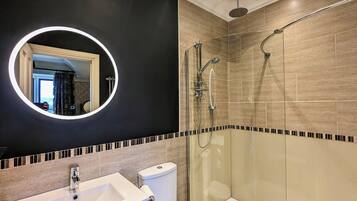 A modern bathroom with a round mirror, a shower, and a toilet.