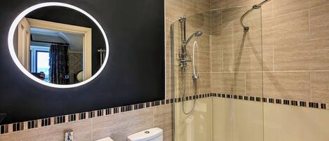 A modern bathroom with a round mirror, a shower, and a toilet.