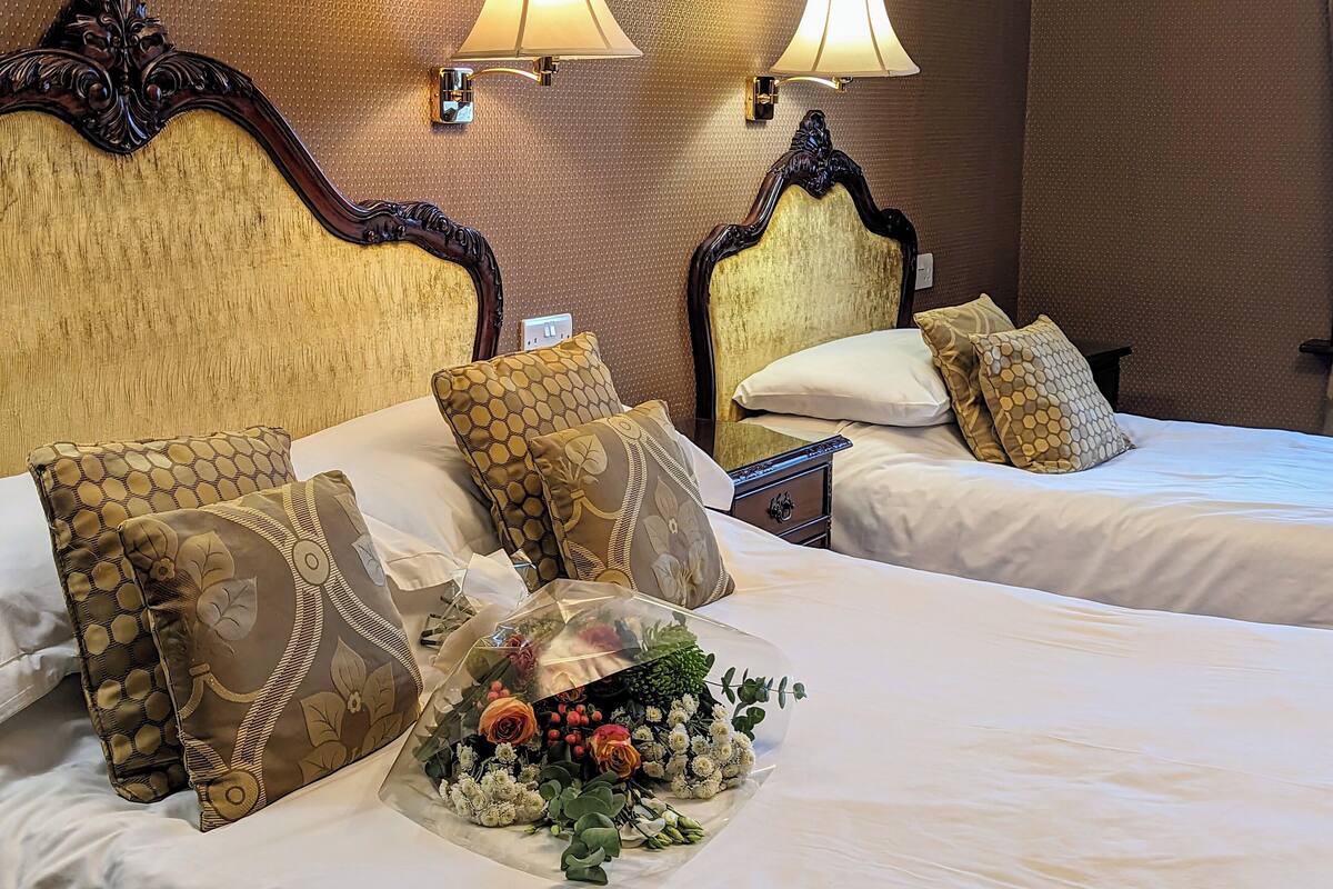 A hotel room with two beds, ornate headboards, and wall-mounted lamps.
