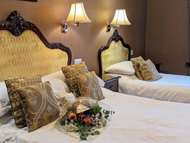 Quarto de hotel com duas camas, cabeceiras elaboradas e luminárias fixadas na parede.