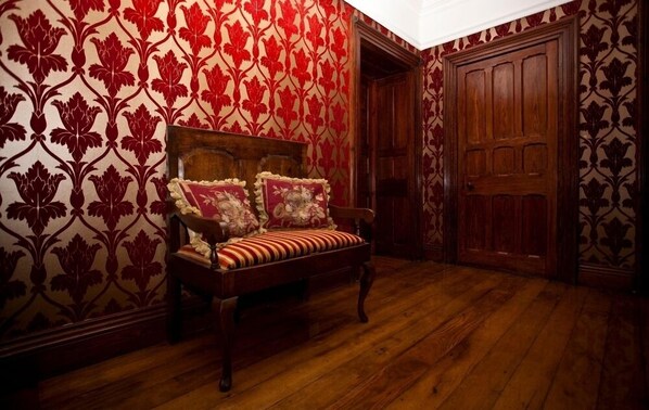 Una habitación con un banco de madera, papel tapiz rojo con estampado y una puerta de madera.
