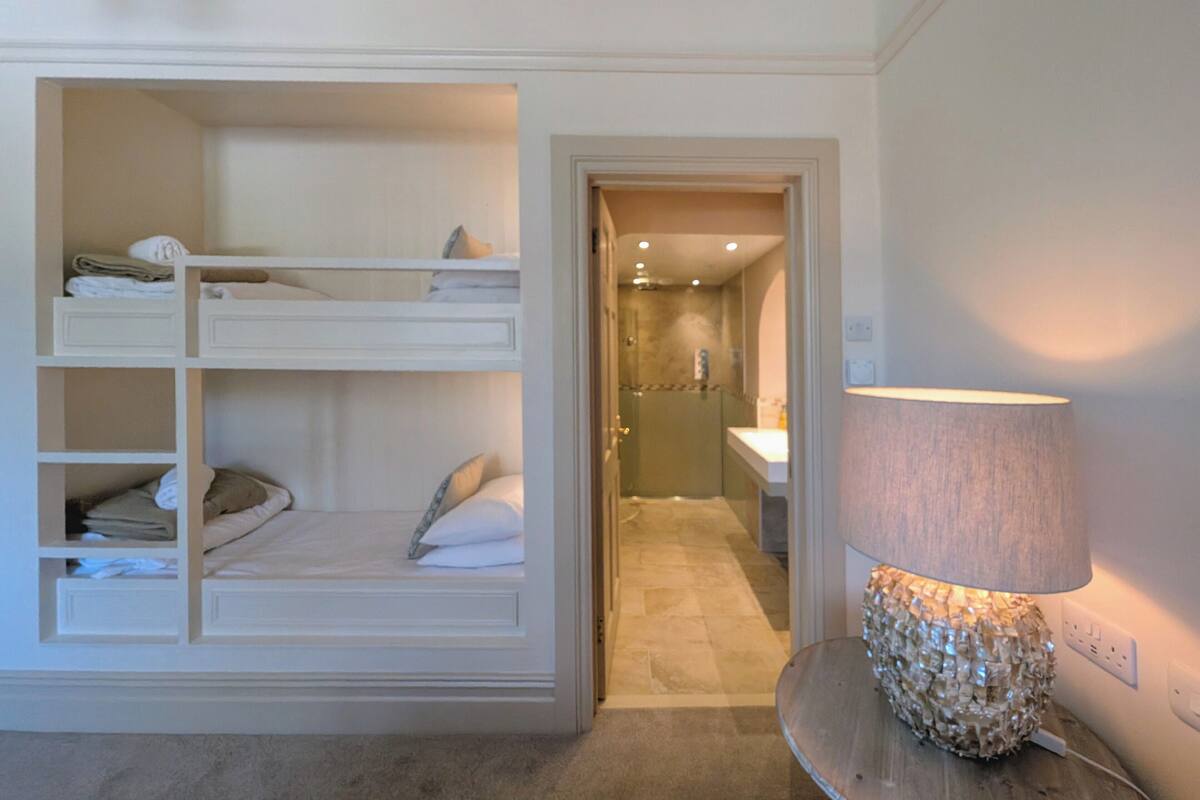 A bedroom with bunk beds, a bedside table with a lamp, and a bathroom visible through an open door.