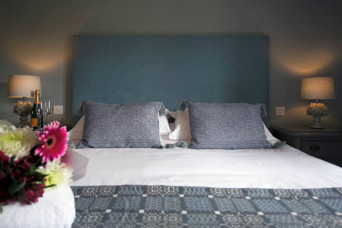 A hotel room with a large bed, two nightstands, a blue headboard, and a vase of flowers.