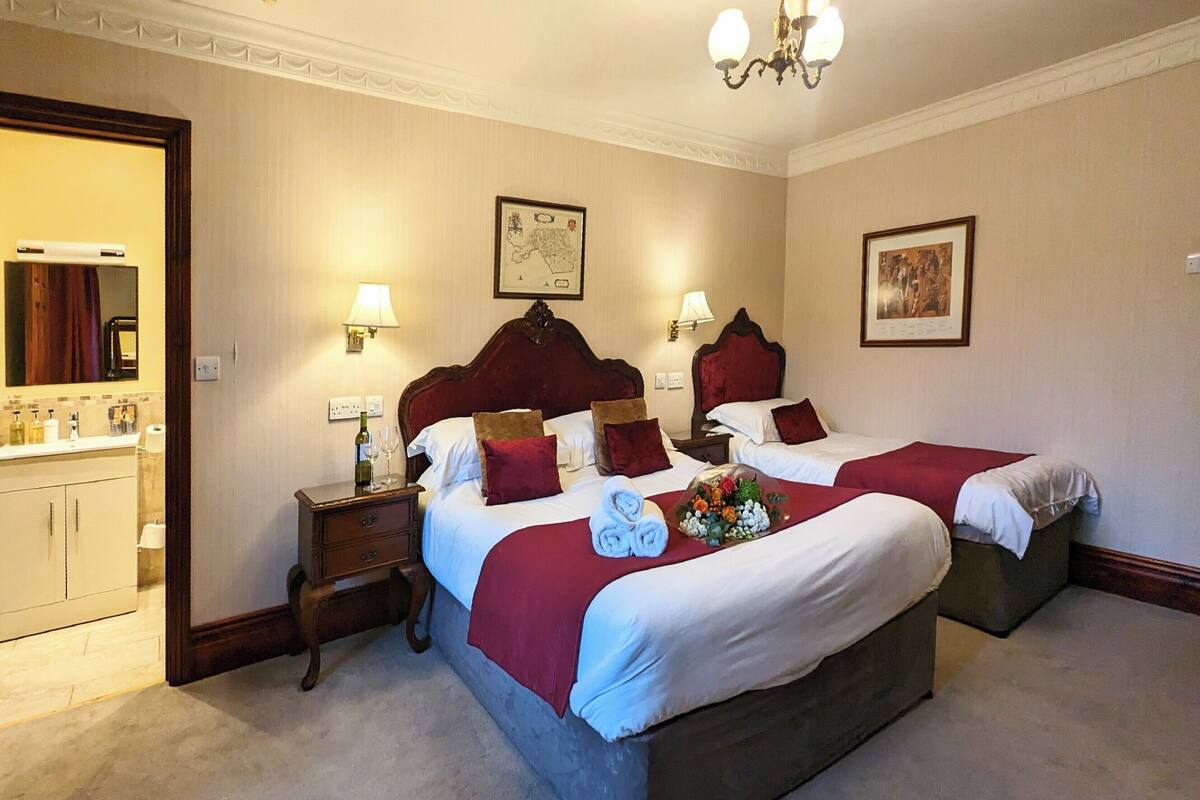 A hotel room with two beds, a bathroom, and a chandelier.