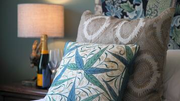A neatly arranged room with a patterned pillow, a lamp, and a bottle of champagne on a wooden side table.