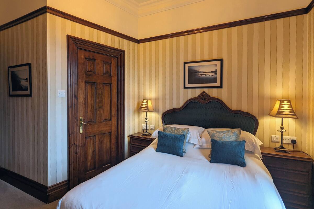 A hotel room with a large bed, two bedside tables with lamps, a wooden door, and striped wallpaper.