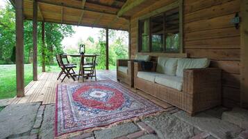 A covered porch with a wooden bench and a table, a woven sofa, and a patterned rug.