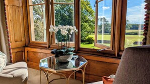 Una habitación con un ventanal grande, suelo de madera, una mesa de vidrio con una planta y una silla.
