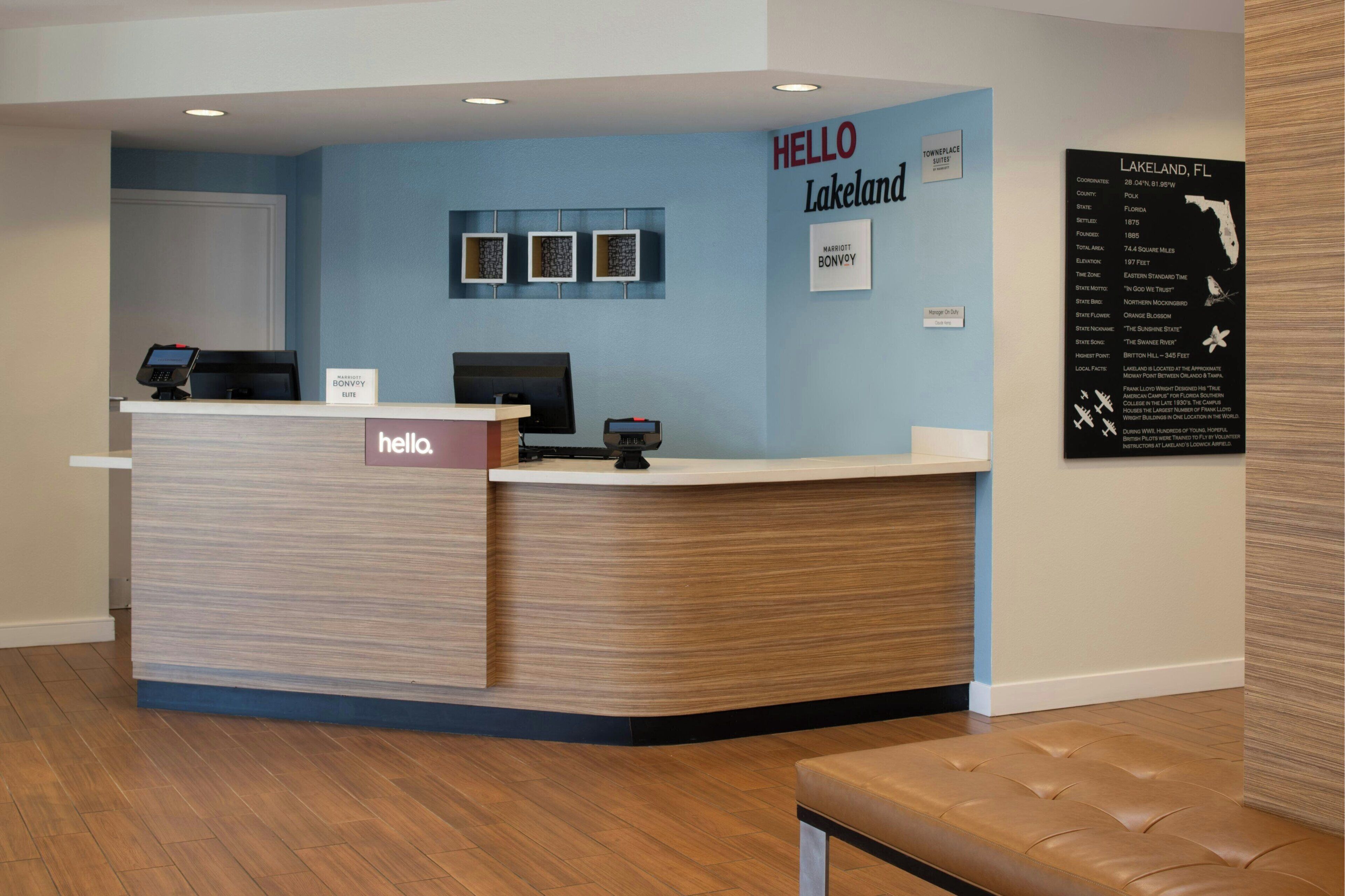 Uma área de recepção de hotel com um balcão de madeira, um letreiro com a inscrição 'hello Lakeland' e um mapa de Lakeland, FL.