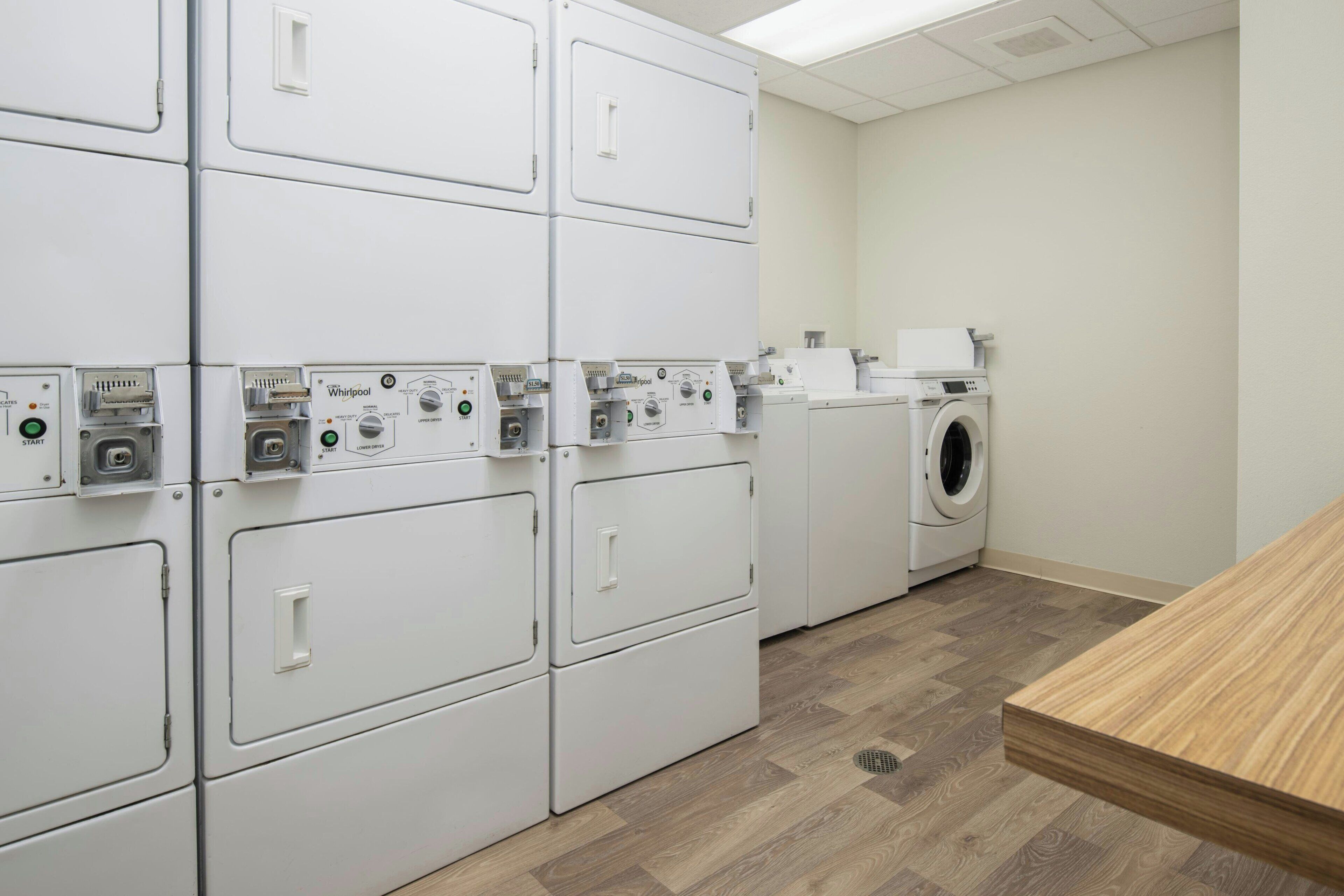 A laundry room with multiple stacked washers and dryers, a wooden table, and a vented ceiling.