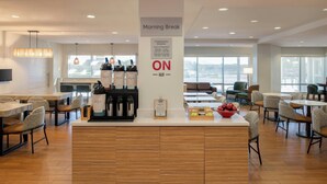 Un espace moderne dédié au petit-déjeuner, avec un comptoir central, des coins repas et une vue sur l’extérieur.