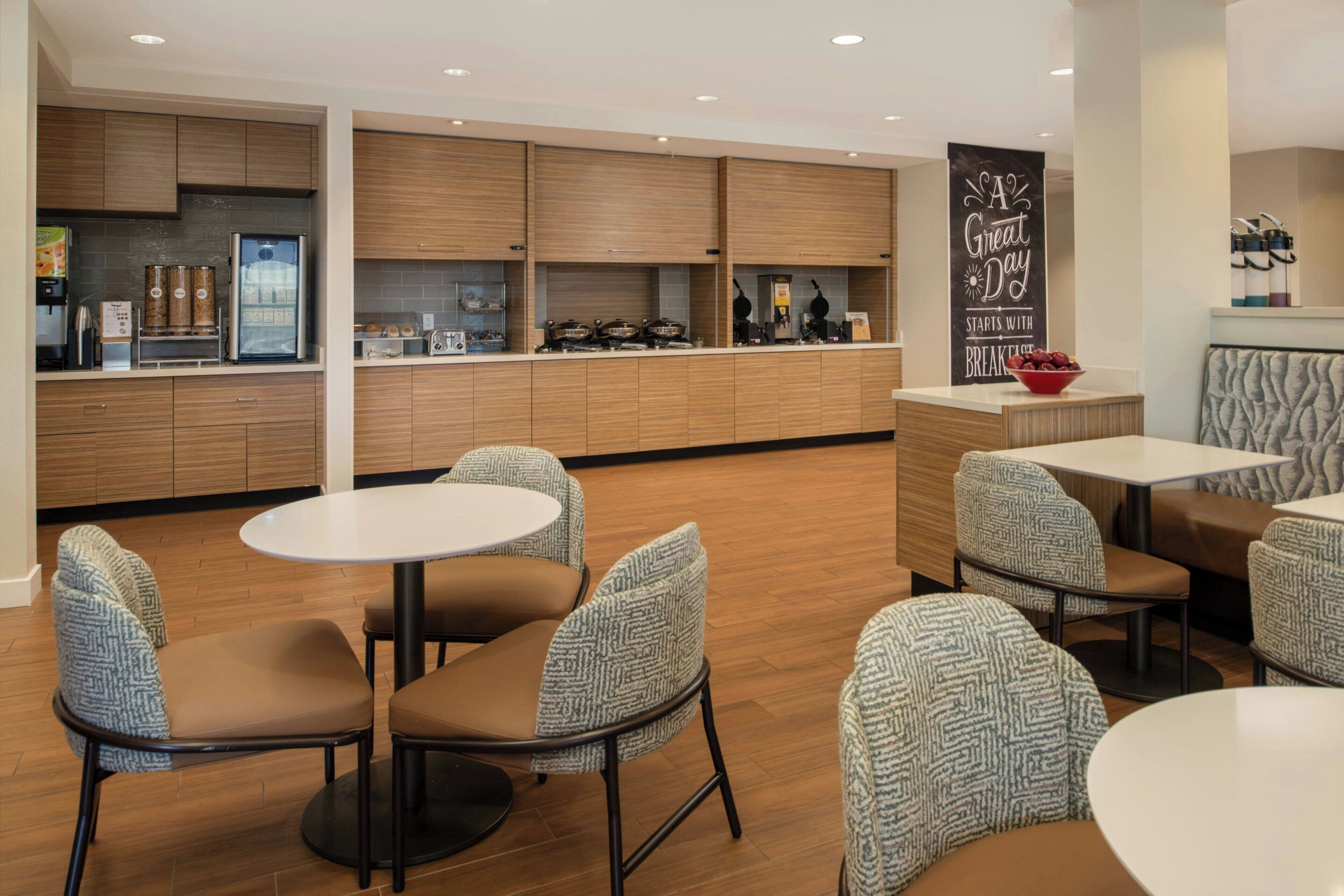 A modern breakfast area with wooden cabinets, a coffee machine, and seating with patterned chairs.