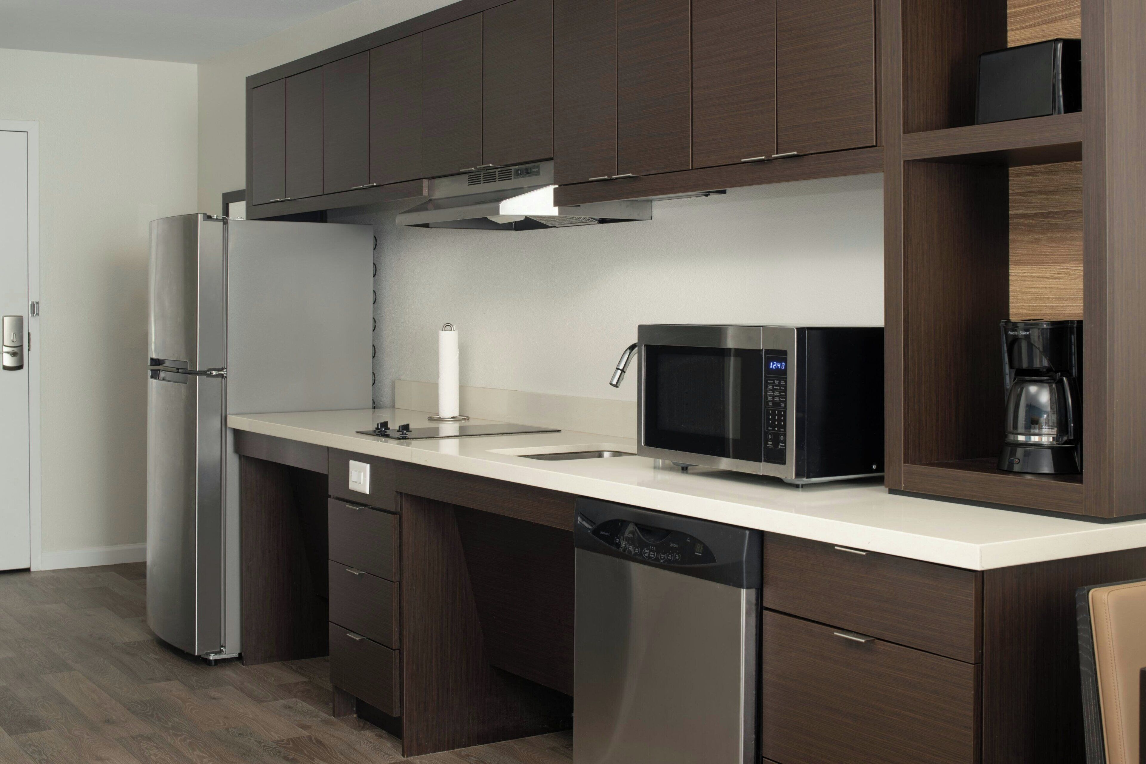 A modern kitchen with dark wood cabinets, stainless steel appliances, and a white countertop.