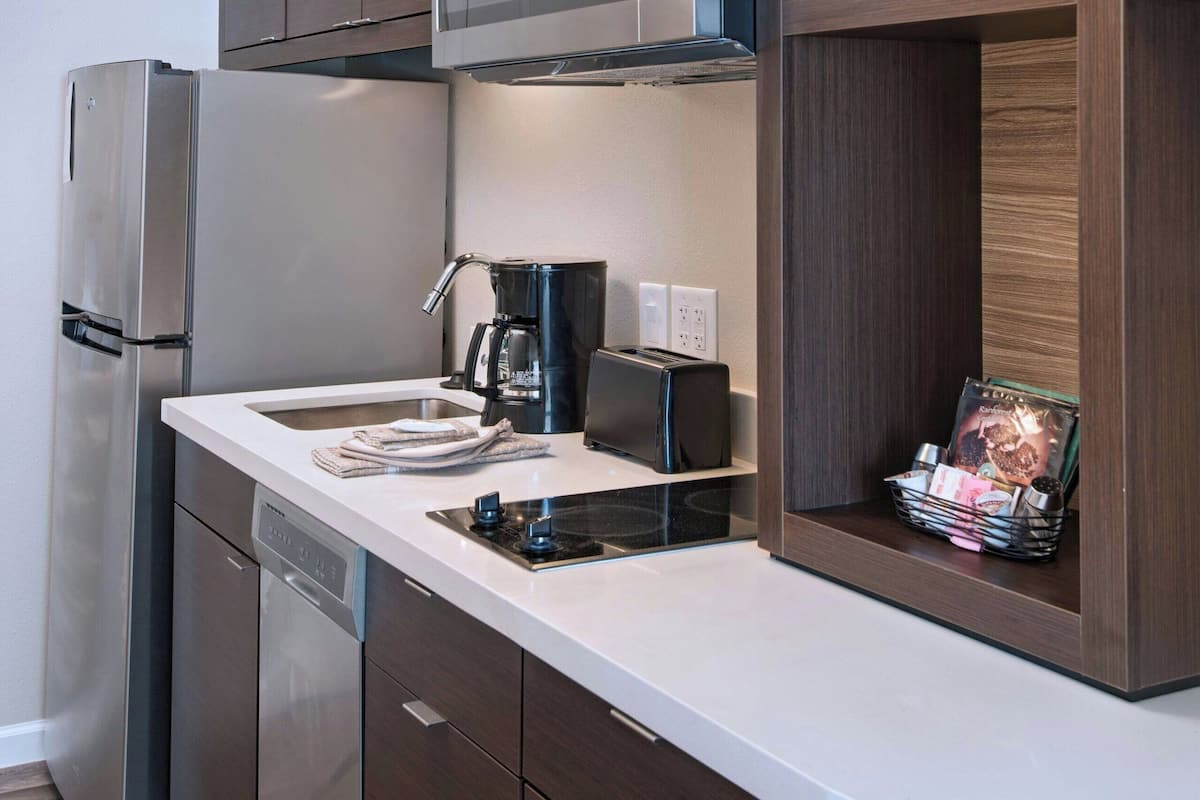 Una cocina moderna con un refrigerador de acero inoxidable, un microondas integrado y una cafetera sobre la encimera.