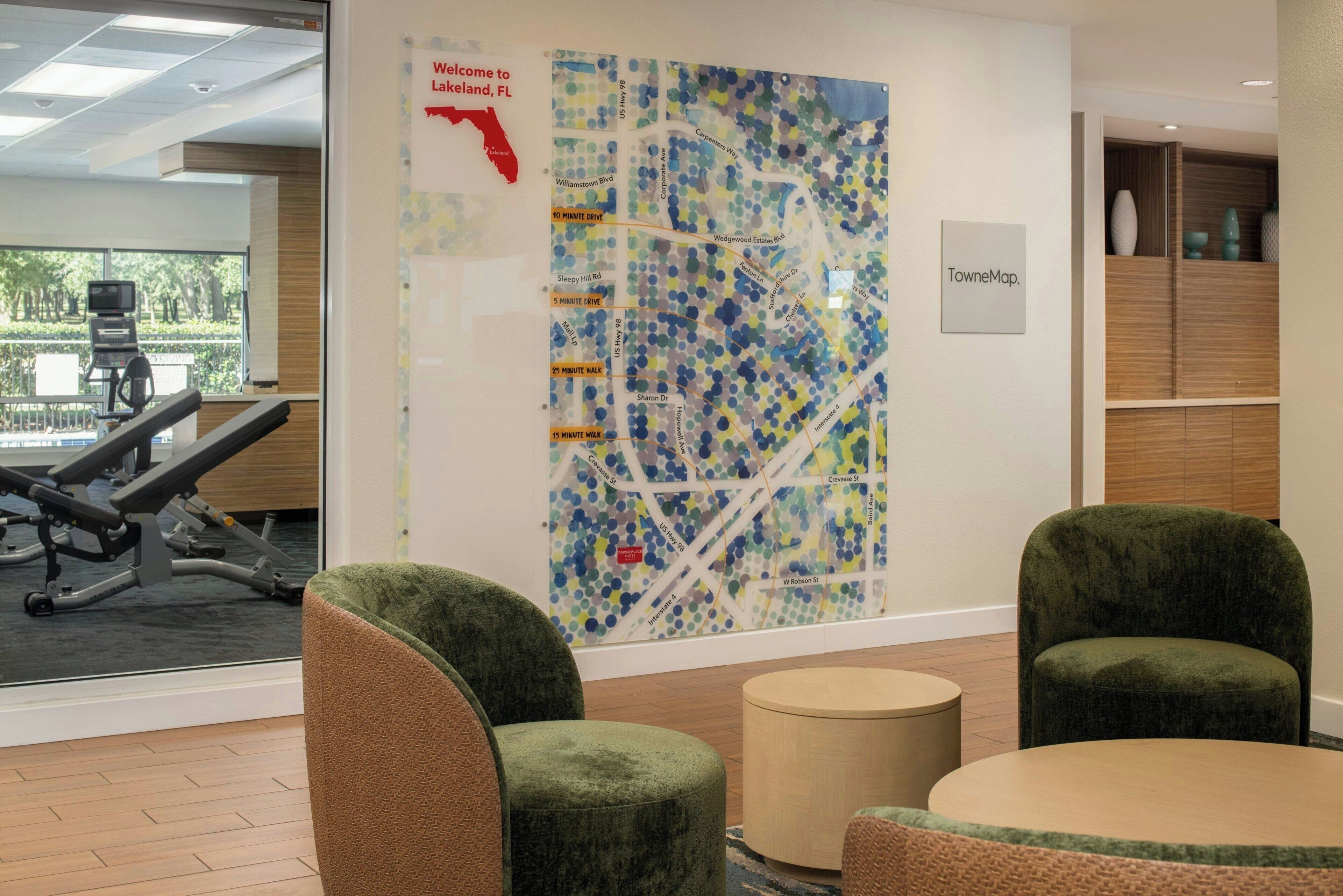 A modern office space with a large map on the wall, green upholstered chairs, a small round table, and a treadmill in the background.