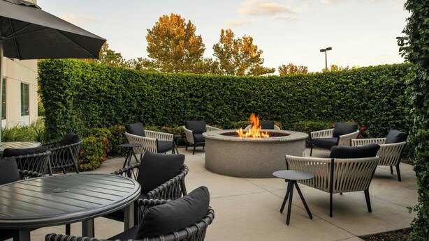 Une terrasse extérieure avec des tables rondes et des chaises en osier, un foyer central et un mur végétal.