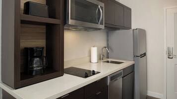 A modern kitchen with dark wood cabinets, a stainless steel refrigerator, a built-in microwave, a coffee maker, and a dishwasher.