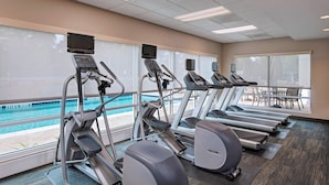 Une salle de sport équipée de tapis de course, de vélos elliptiques et offrant une vue sur la piscine.