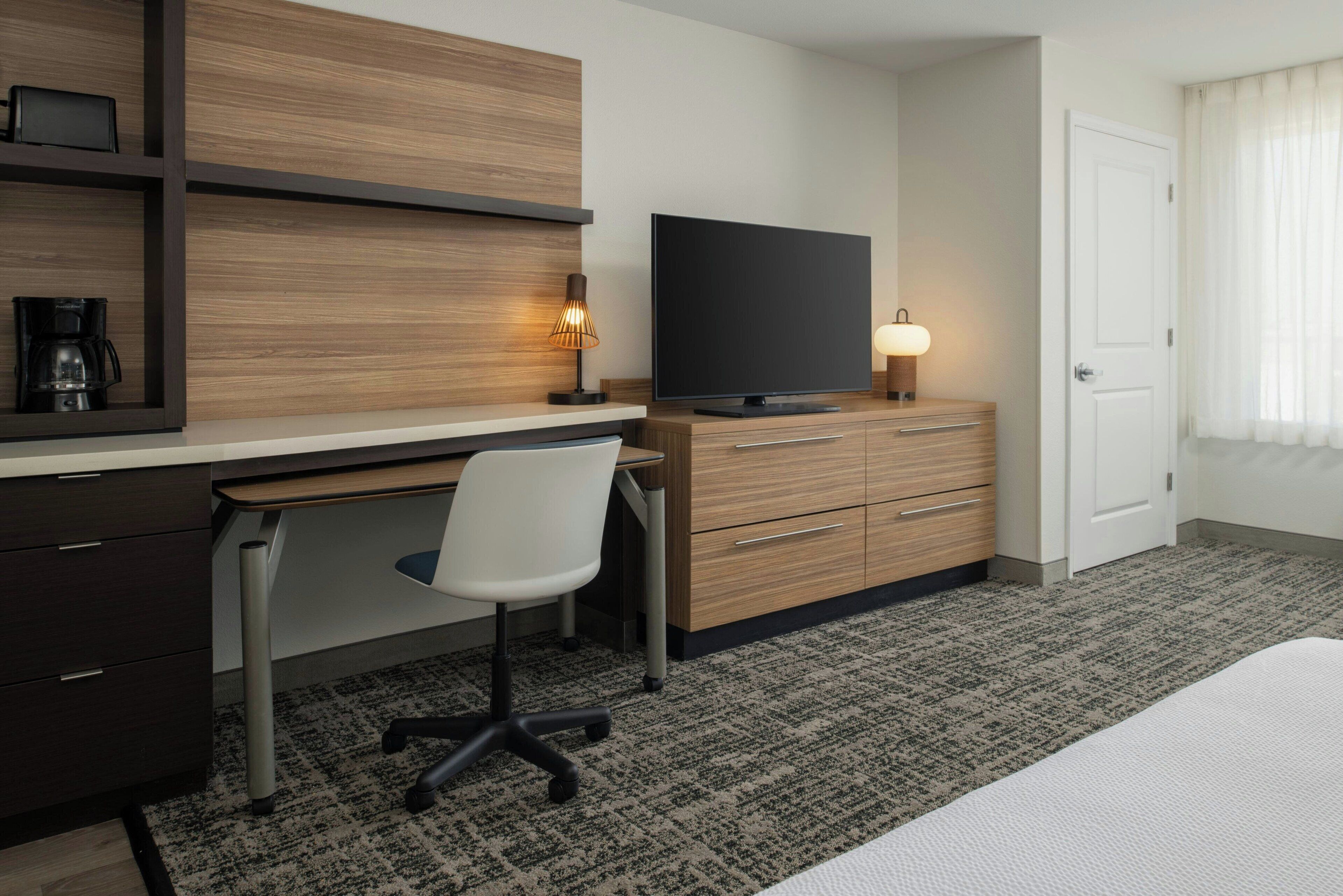 Una habitación de hotel con escritorio de madera, televisión, silla, cómoda y cama.