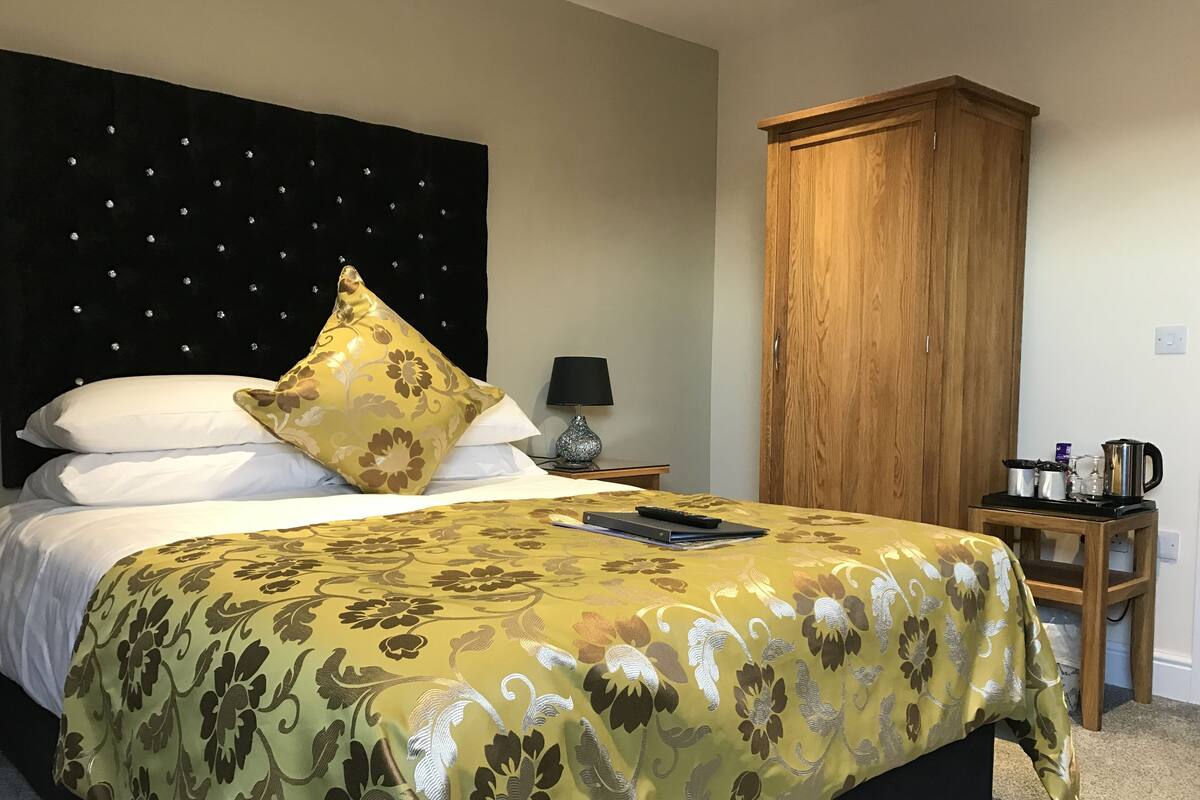 Una cama bien hecha con una colcha estampada con motivos florales, una lámpara de noche y un armario de madera.