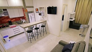 A compact living space with a kitchenette, a dining area with bar stools, a sofa, and a TV mounted on the wall. - Rio Spot Apartments U033 (Rio de Janeiro)