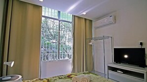 A hotel room with a bed, a TV, a window with curtains, and an air conditioning unit. - Rio Spot Apartments U033 (Rio de Janeiro)