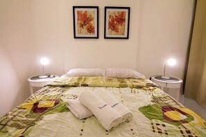 A neatly made bed with a floral quilt, two framed artworks on the wall, and bedside lamps.