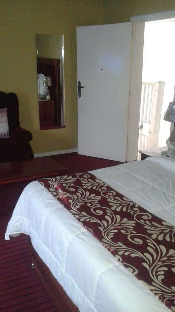 A bedroom with a bed, a door, a mirror, and a chair.