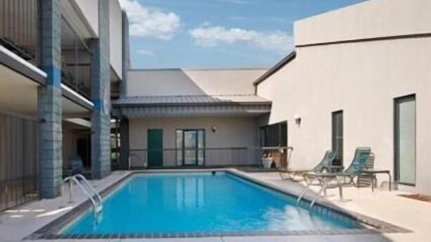 A swimming pool with lounge chairs, a building with a flat roof, and a clear sky.